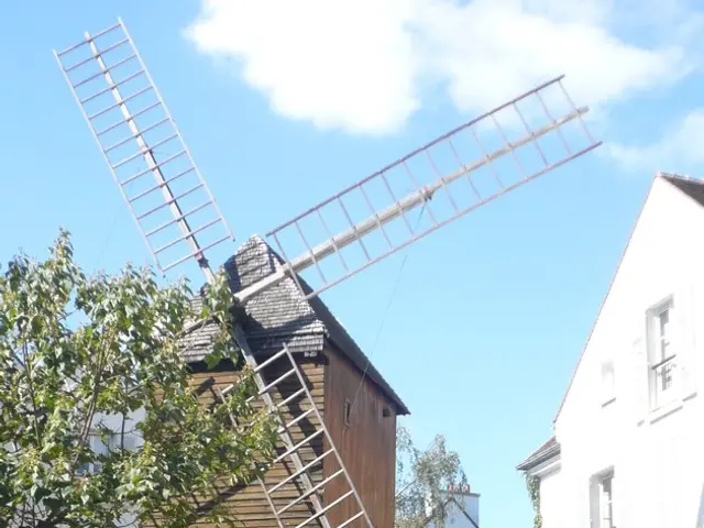 In this picture we can see a windmill, few buildings, trees and metal rods, and also we can find...